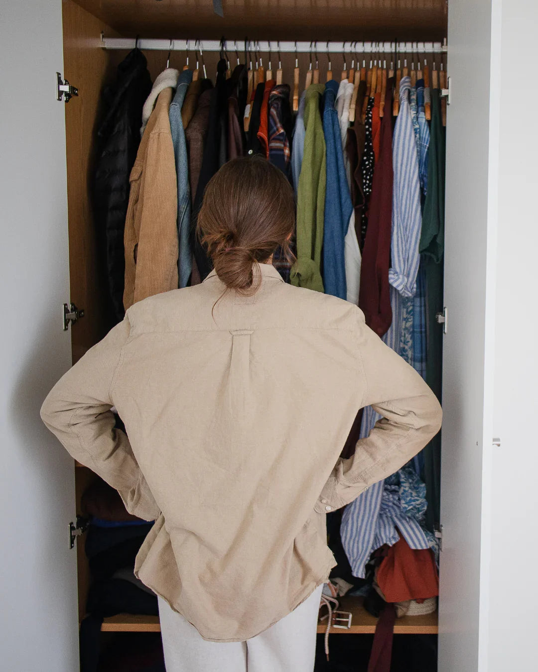Mujer de espaldas frente a armario abierto con ropa colgada, organización de closet