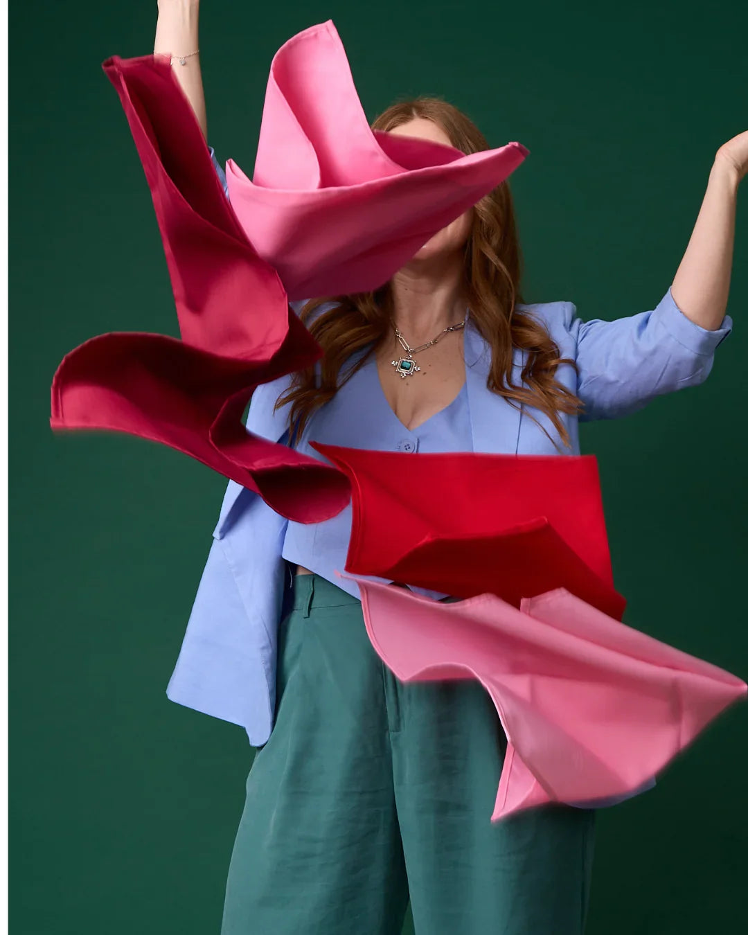 Mujer con blazer azul lanza pañuelos rosa y fucsia al aire, fondo verde elegante.